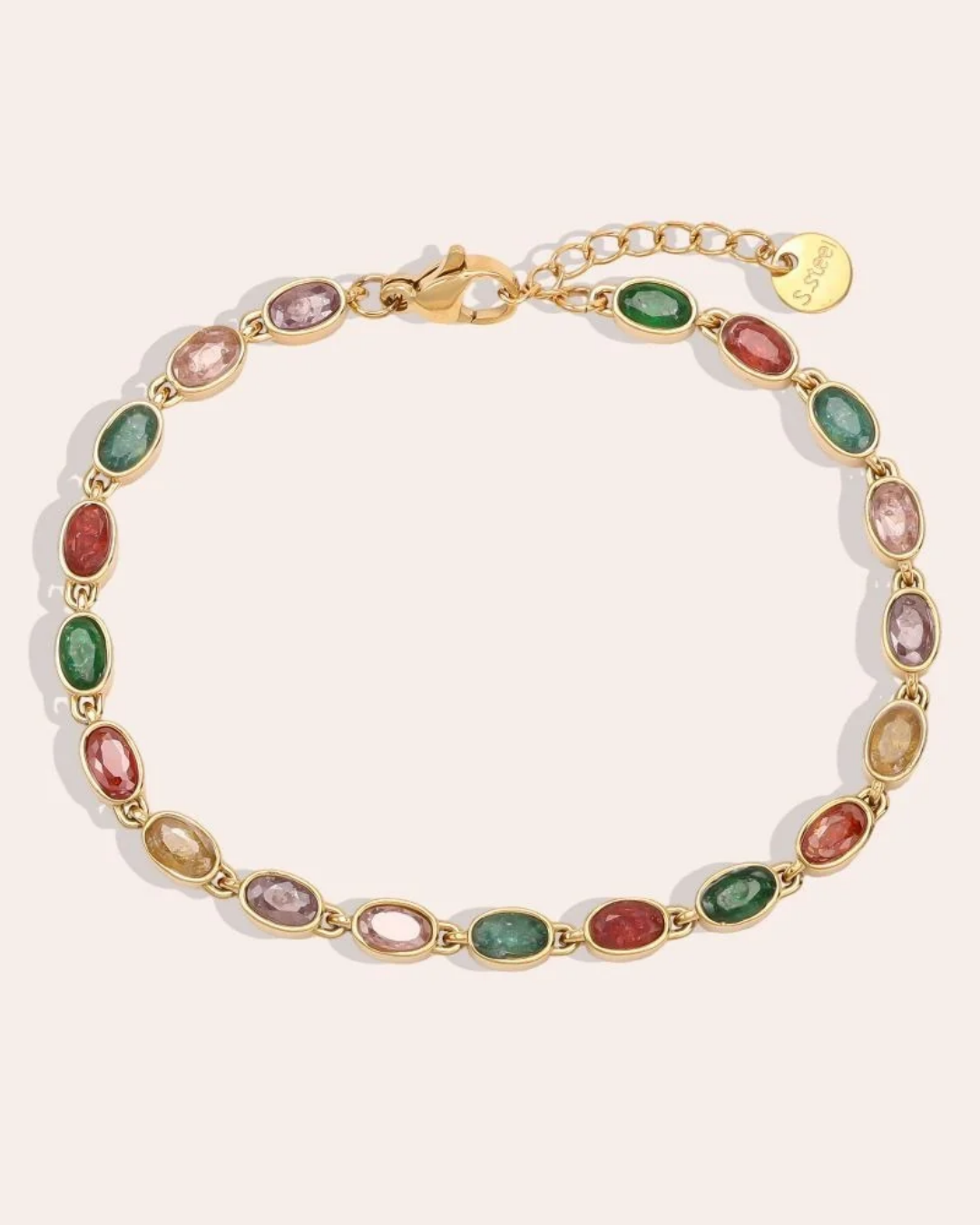 Armband mit bunten Steinen von Dottilove vor beigen Hintergrund. Das Armband selbst ist gold mit bunten Steinen in grün, rot lila und gelb.