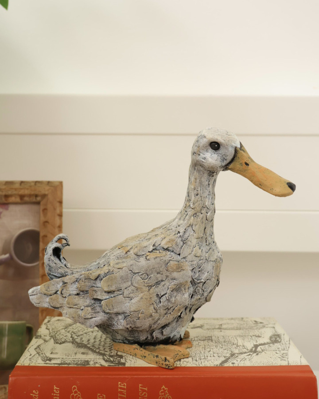 Enten Statue "Lily" steht auf Büchern und schaut nach rechts. neben der Statue ist ein Bild.