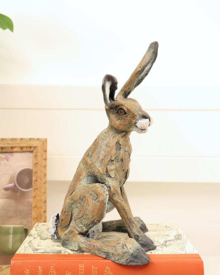 Hasen Statue "Rowan" sitzt auf Büchern und schaut nach rechts. Der Hase sitzt auf Büchern und neben dem Hasen ein Bild.