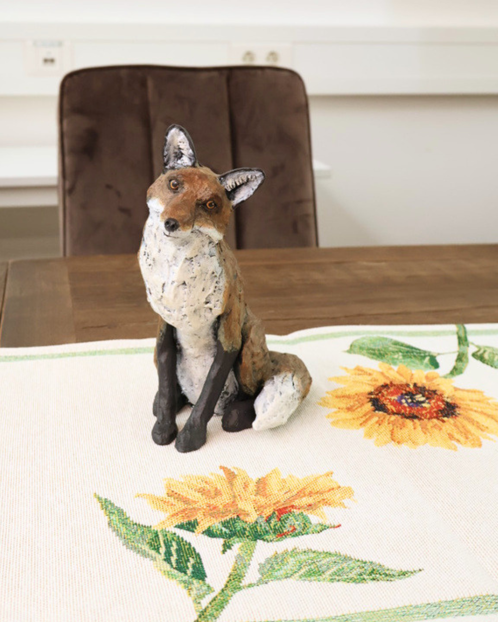Fuchs Figur "Autumn" von Wrendale Designs auf einem dekorierten Esstisch. Der Fuchs guckt mit einem angewinkelten Kopf in die Kamera. 