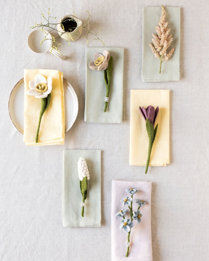 Filzblumen von Gry & Sif als Tischdekoration auf gefalteten Servietten in sanften Frühlingsfarben.