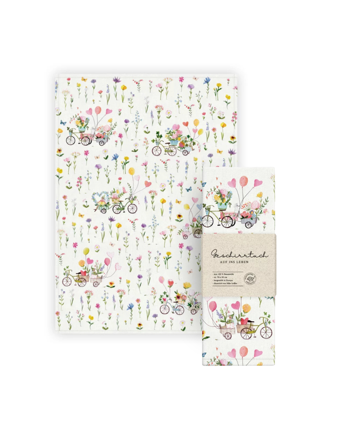 Geschirrtuch „Auf ins Glück“ vom Grätz Verlag mit floralen Mustern und kleinen Fahrrädern auf hellem Hintergrund, gestaltet von Silke Leffler.