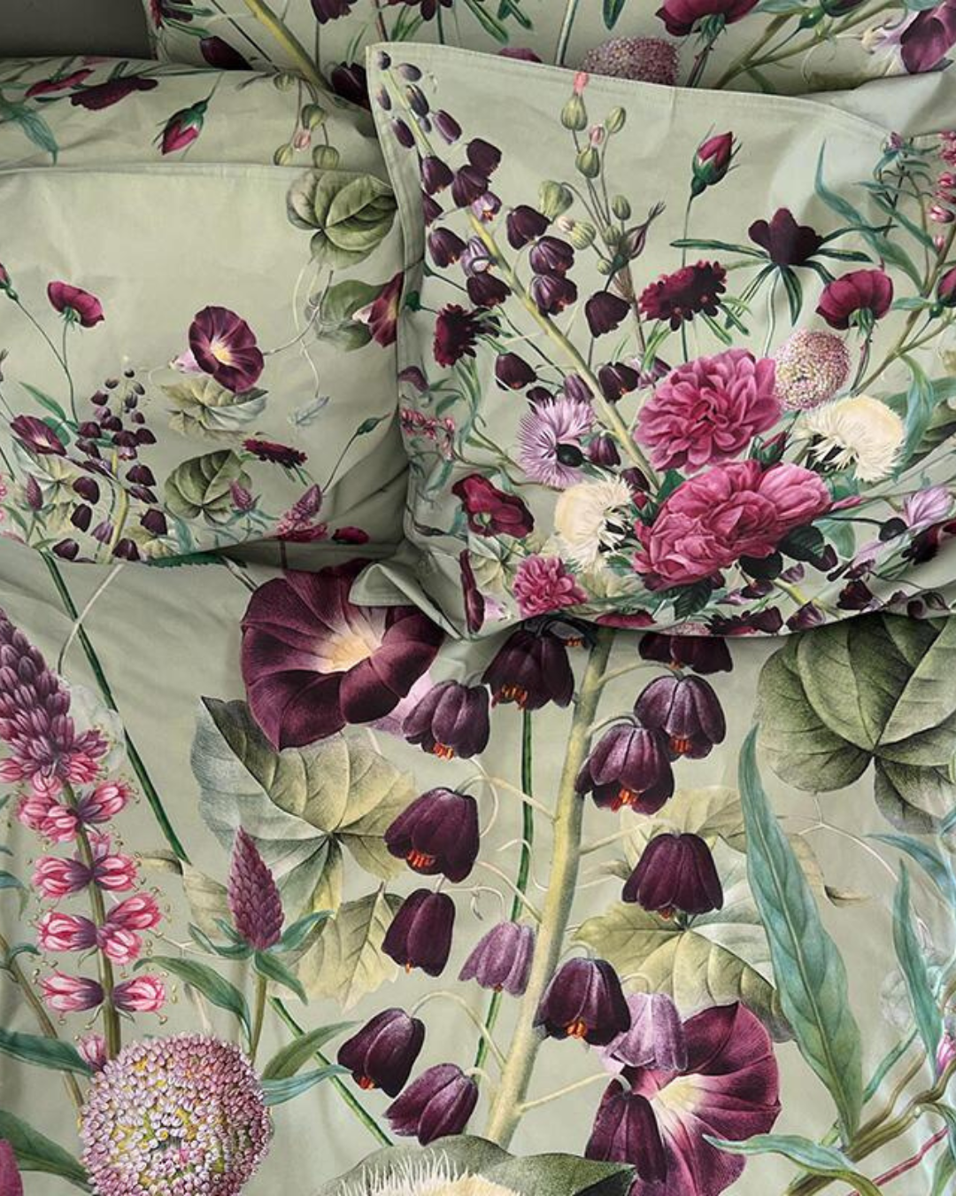 Kissenbezüge Blossom Garden mit Blumenmotiven in Rosa, Lila und Grün, gestapelt auf einem Bett.

