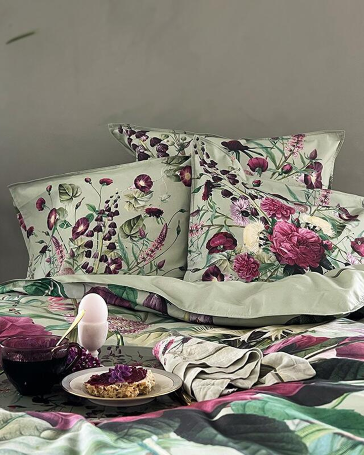 Bett mit Bettwäsche Blossom Garden, Kissen und Frühstückstablett mit Tasse und Teller, gemütliche Atmosphäre.