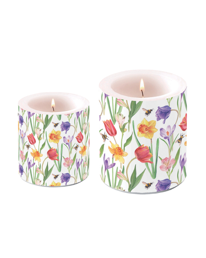 Kleine und große zylindrische Kerze mit Frühlingsblumenmotiv (Tulpen, Narzissen, Krokusse) der Marke Ambiente, beide brennend, nebeneinander auf weißem Hintergrund.