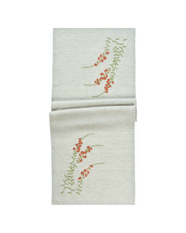 Der Blumen Tischläufer „Sunny Meadow“ von Sander in Koralle zeigt eine feine, gestickte Blumenranke auf hellem Stoff.