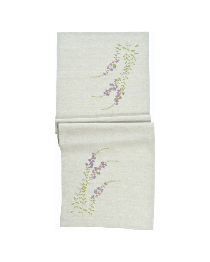 Der Blumen Tischläufer „Sunny Meadow“ von Sander in Lila ist mit einer zarten, gestickten Blumenranke auf naturfarbenem Stoff gestaltet.