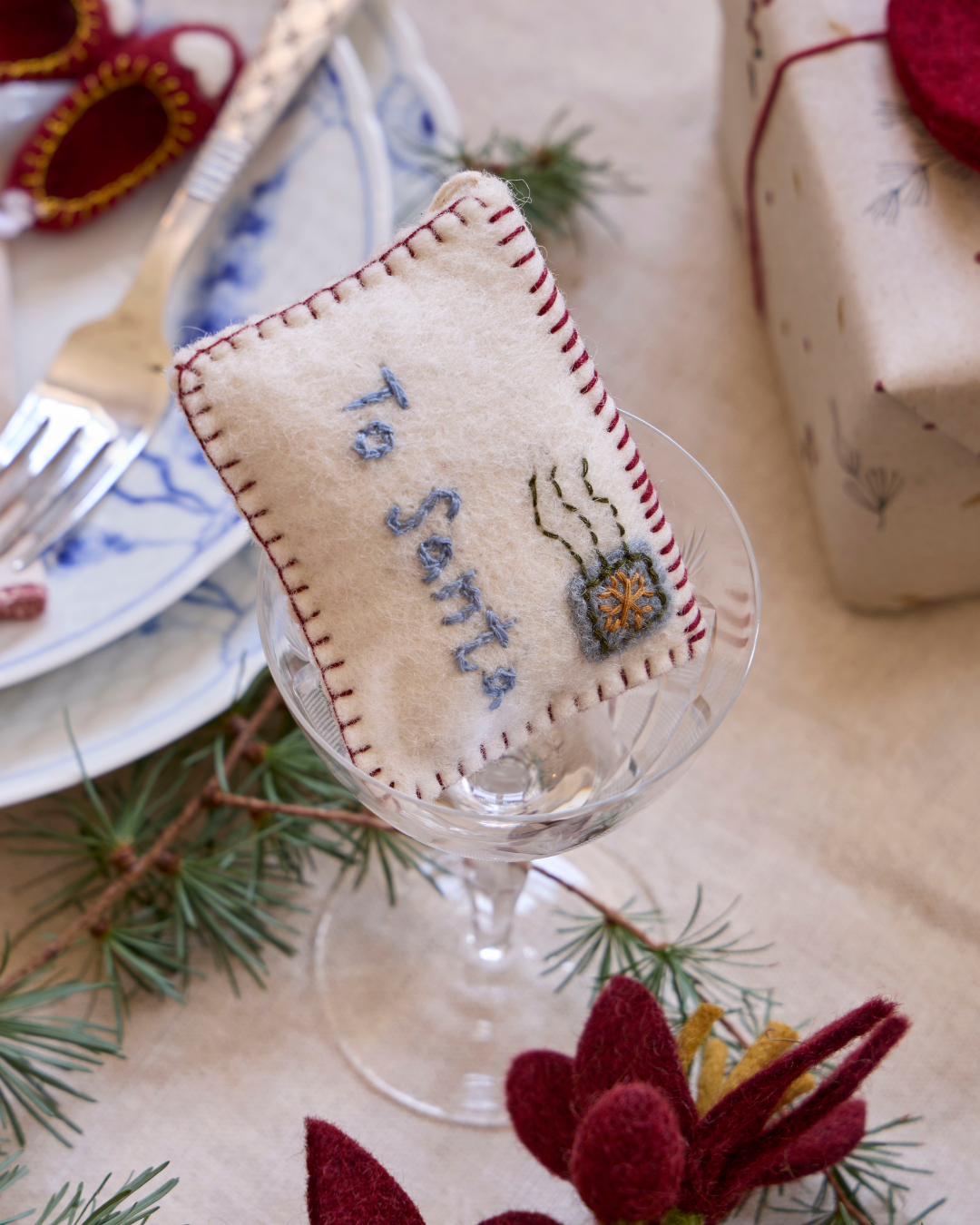 Filzanhänger "Letter to Santa" in einem Glas, welches auf einem weihnachtliche eingedeckten und geschmückten Holztisch steht.