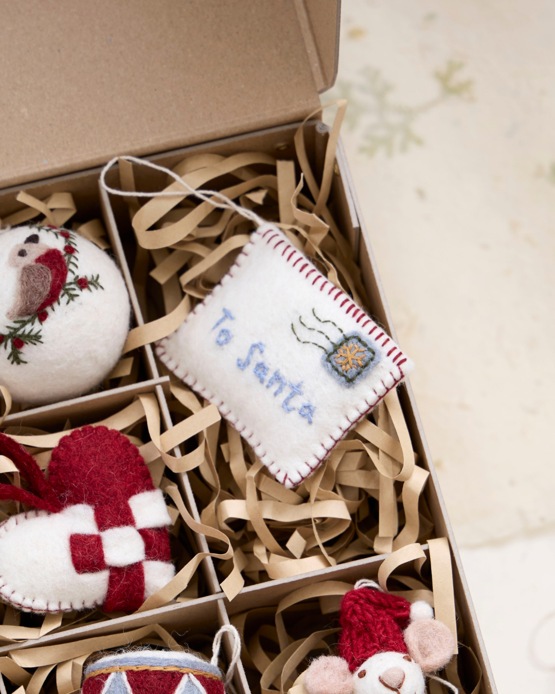 Filzanhänger "Letter to Santa" auf Packpapier liegend in einem Karton mit weiteren Filzanhängern.
