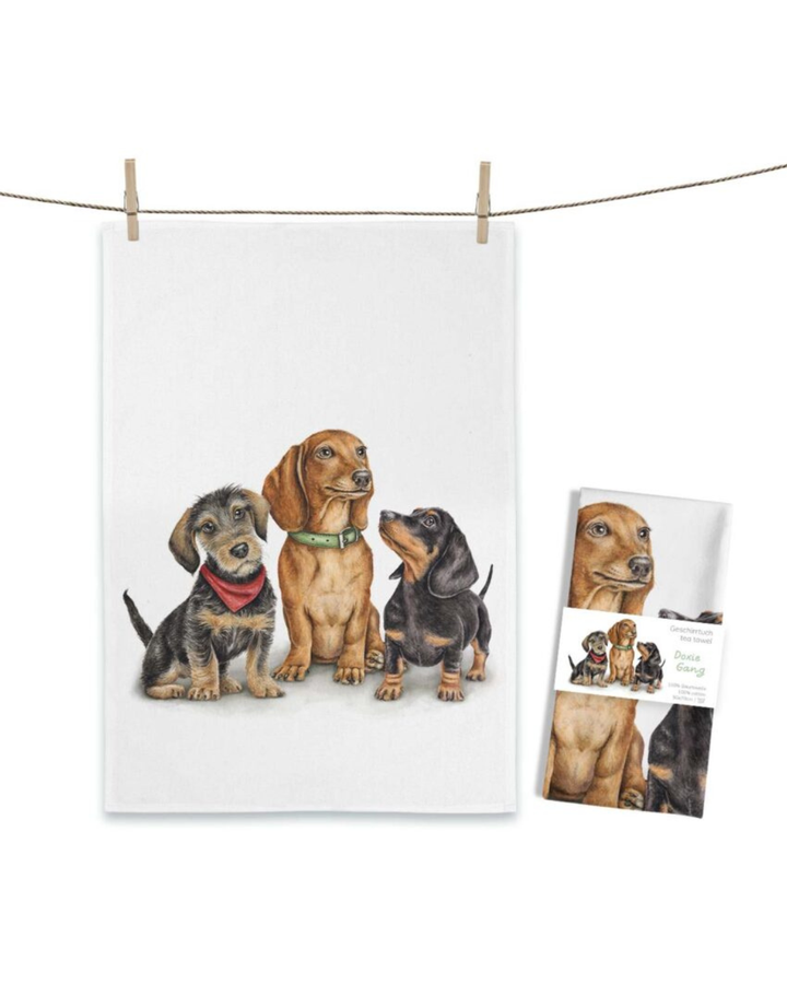 Dackel Geschirrtuch Doxie Gang von Maluu mit drei illustrierten Dackeln nebeneinander auf hellem Hintergrund aufgehängt an einer Leine