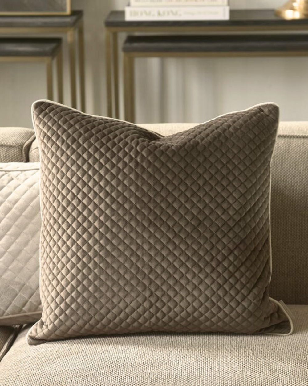 Das Kissen The Classic Club aus braunem Samt von Rivèra Maison ist auf einer braunen Couch dekoriert.