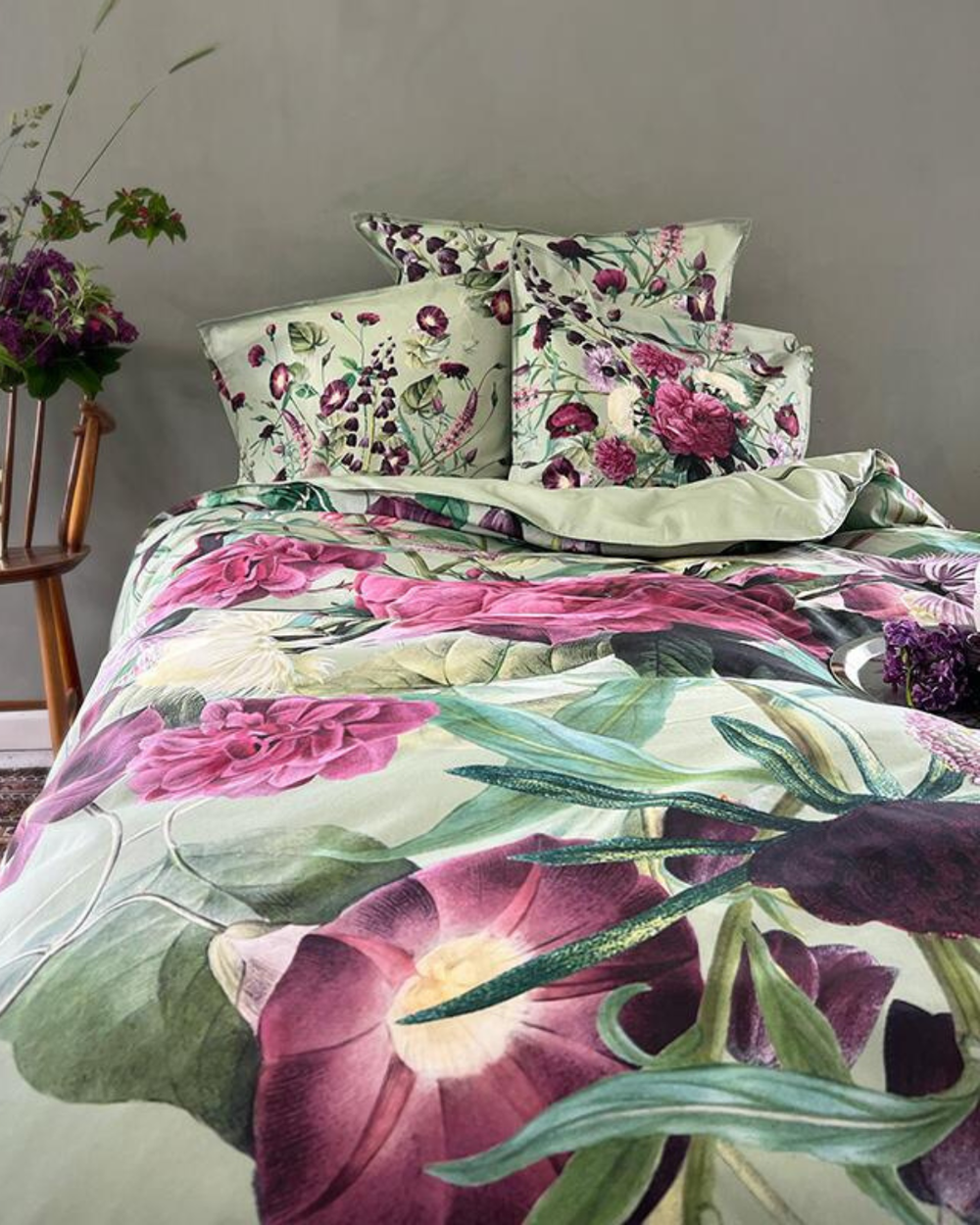 Bett mit Bettwäsche Blossom Garden, Kissen und Decke mit floralem Muster, dekoriert mit frischen Blumen in einer Vase.