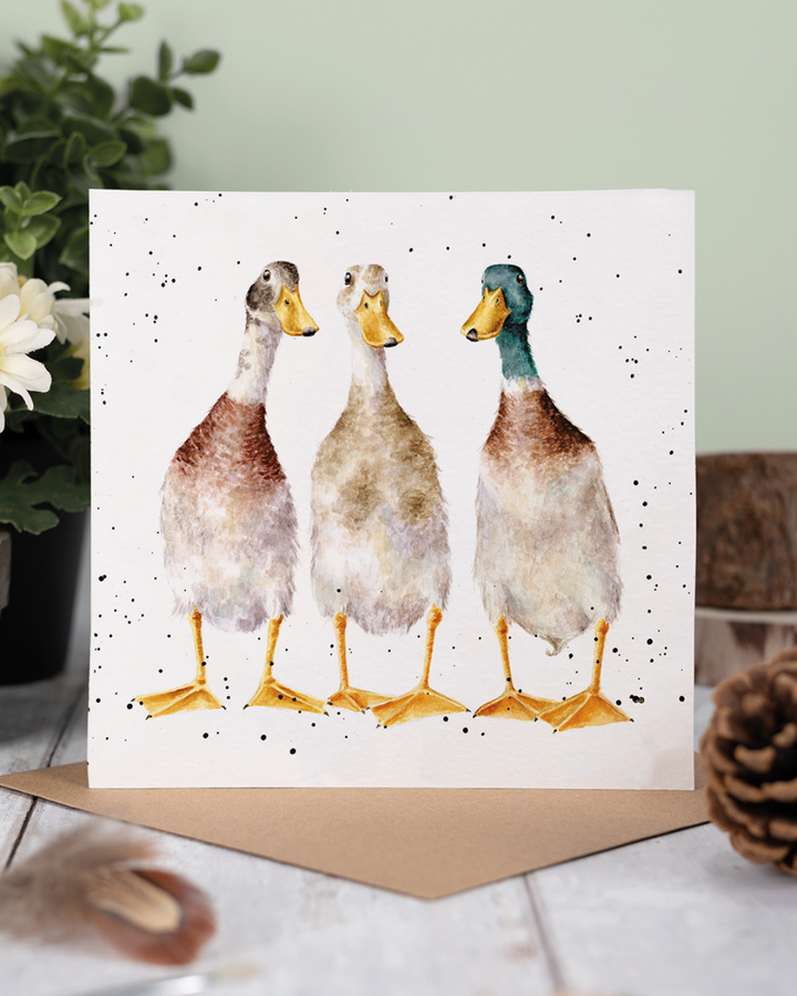 Dekoriertes Produktfoto der Enten Grußkarte „Tall Order“ von Wrendale Designs, aufgestellt auf einem Holzuntergrund mit braunem Umschlag, im Hintergrund grüne Pflanzen und natürliche Deko.