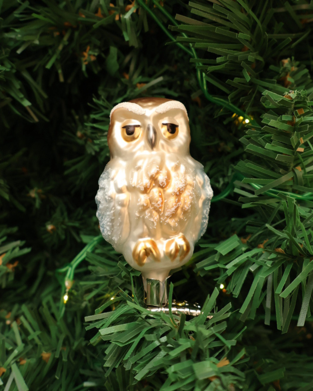 Dekorierter Weihnachtsbaumschmuck "Eule" zum klemmen von Inge Glas hängt an Tannenbaum. Zu sehen ist eine weiß/braun/goldene Eule welche in die Kamera schaut.