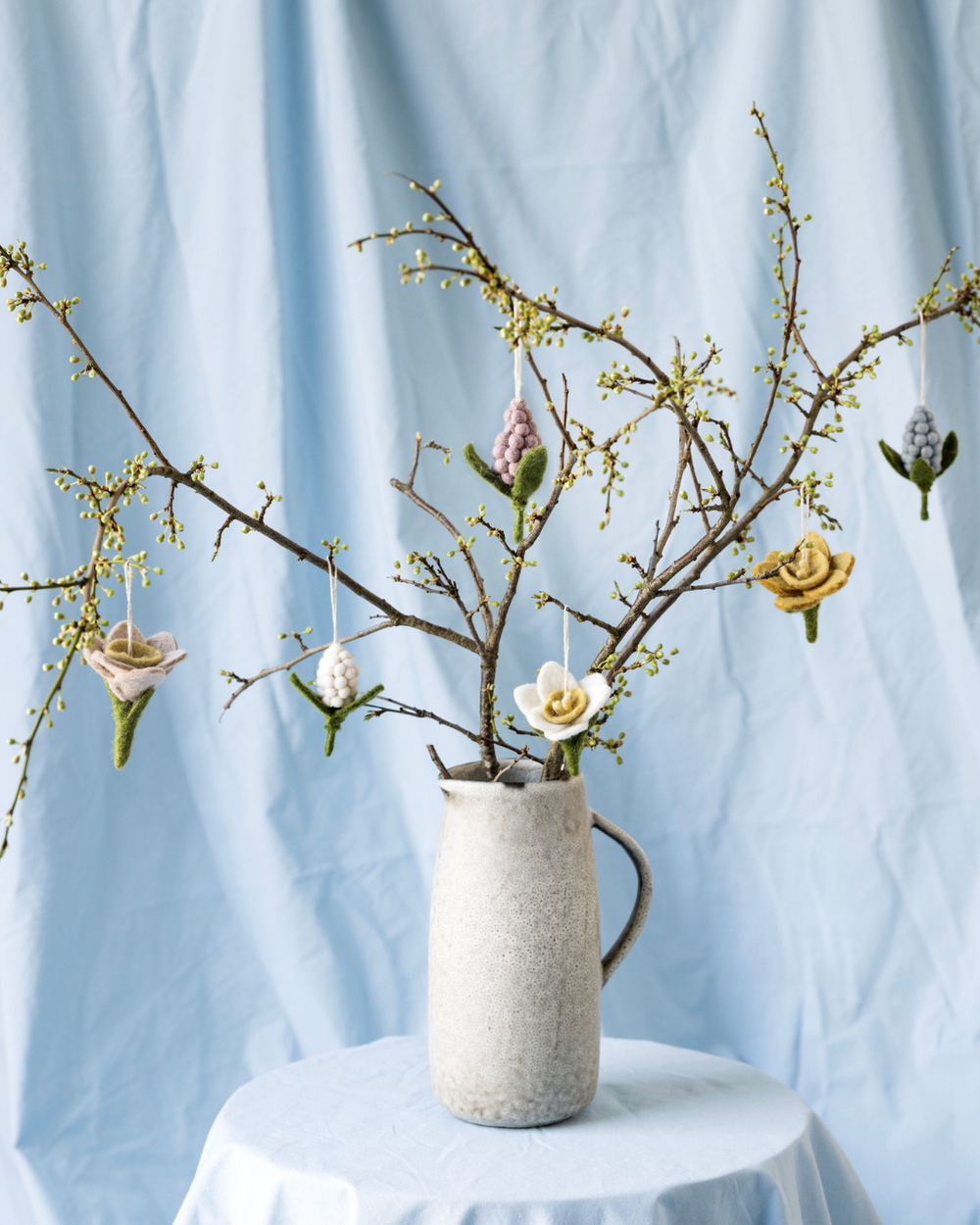 Filzblumen als Anhänger von Gry & Sif, Hyazinthen und Narzissen dekorativ an blühenden Zweigen in einer Keramikvase arrangiert.