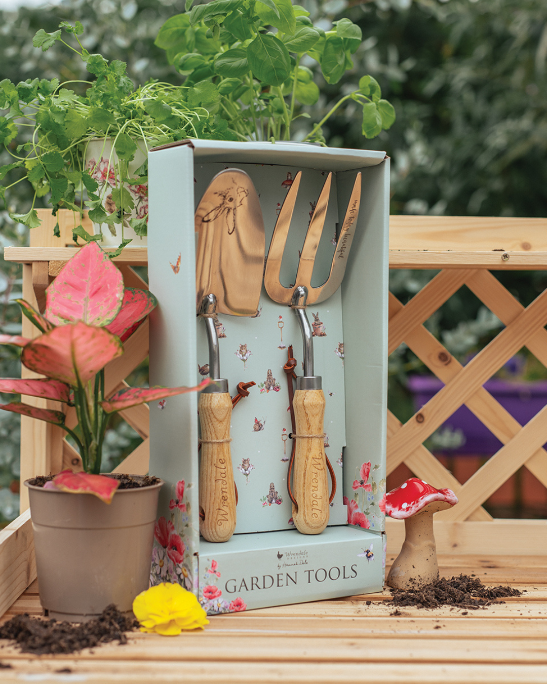 Gartenwerkzeug Fork & Trowel von Wrendale Designs auf Holzuntergrund mit Pflanzen