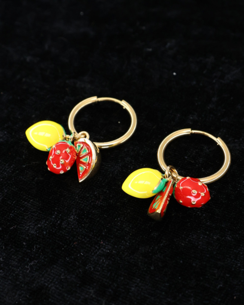 Goldene Ohrringe "Emaille Früchte" von Dottilove mit Zitrone, Erdbeer und wassermelone Anhänger auf schwarzer leicht glitzernder Decke.