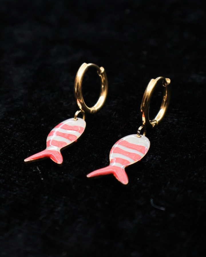 Goldene pink/weiß gestreifte Fisch-Ohrringe von Dottilove auf schwarzer leicht glitzernder Decke.