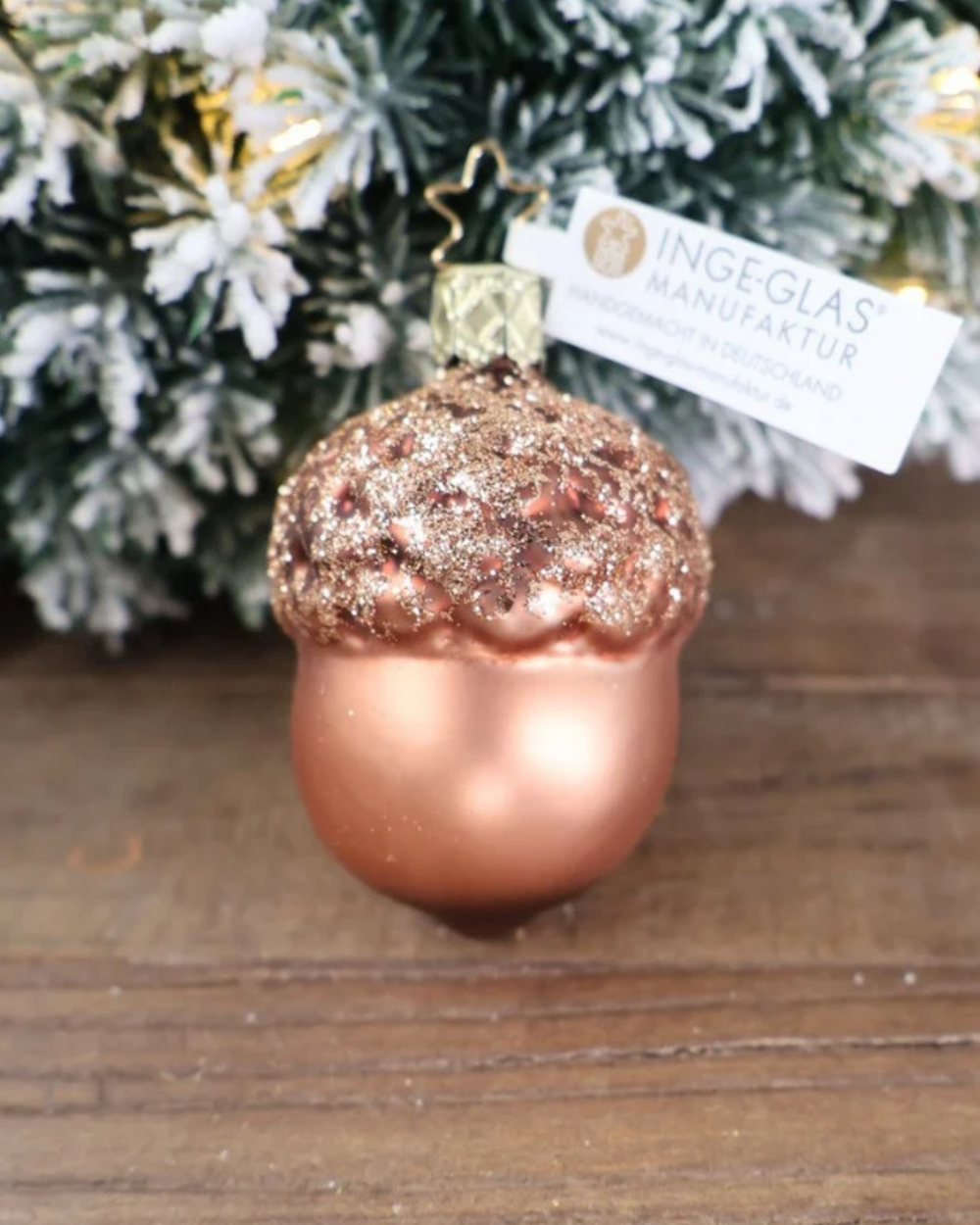 Weihnachtliches großes Eichel Ornament von Inge Glas dekoriert vor weiß gepudertem Tannengrün auf einem Holztisch.