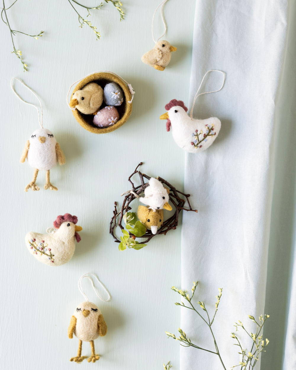 Dekorative Szene mit mehreren Filzanhängern von Gry & Sif, darunter Küken, Hühner und Eier, arrangiert auf hellem Untergrund mit Zweigen.