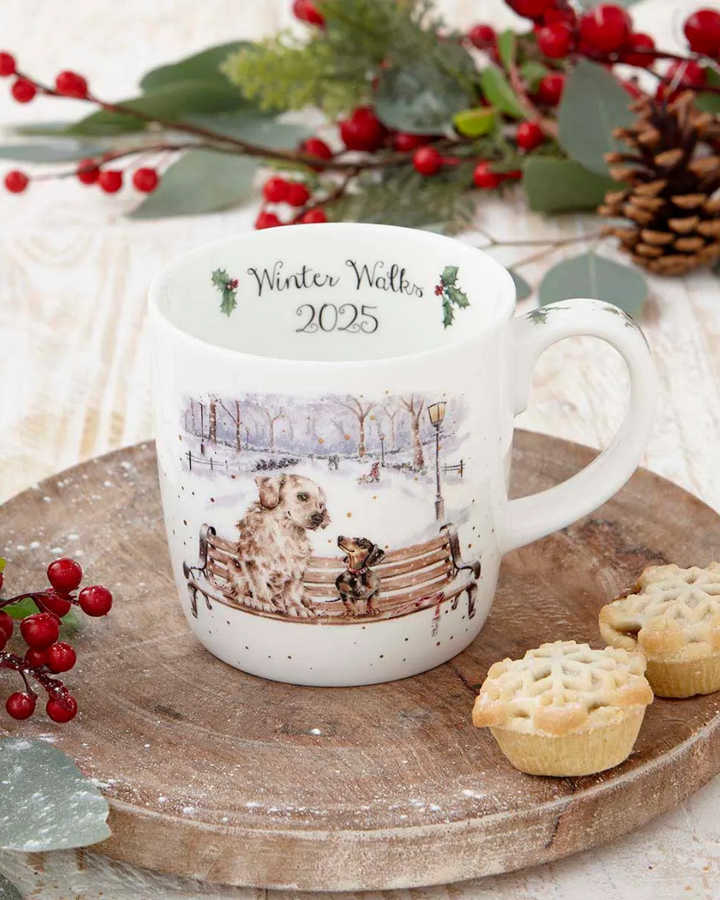 Hunde Jahrestasse 2025 Winter Walks von Wrendale Design dekoriert auf einer Baumstammscheibe mit kleinen Biskuits.