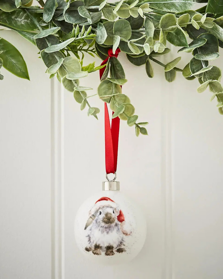 Weiße Porzellankugel von Wrendale Designs mit Kaninchenmotiv und Weihnachtsmütze hängend.