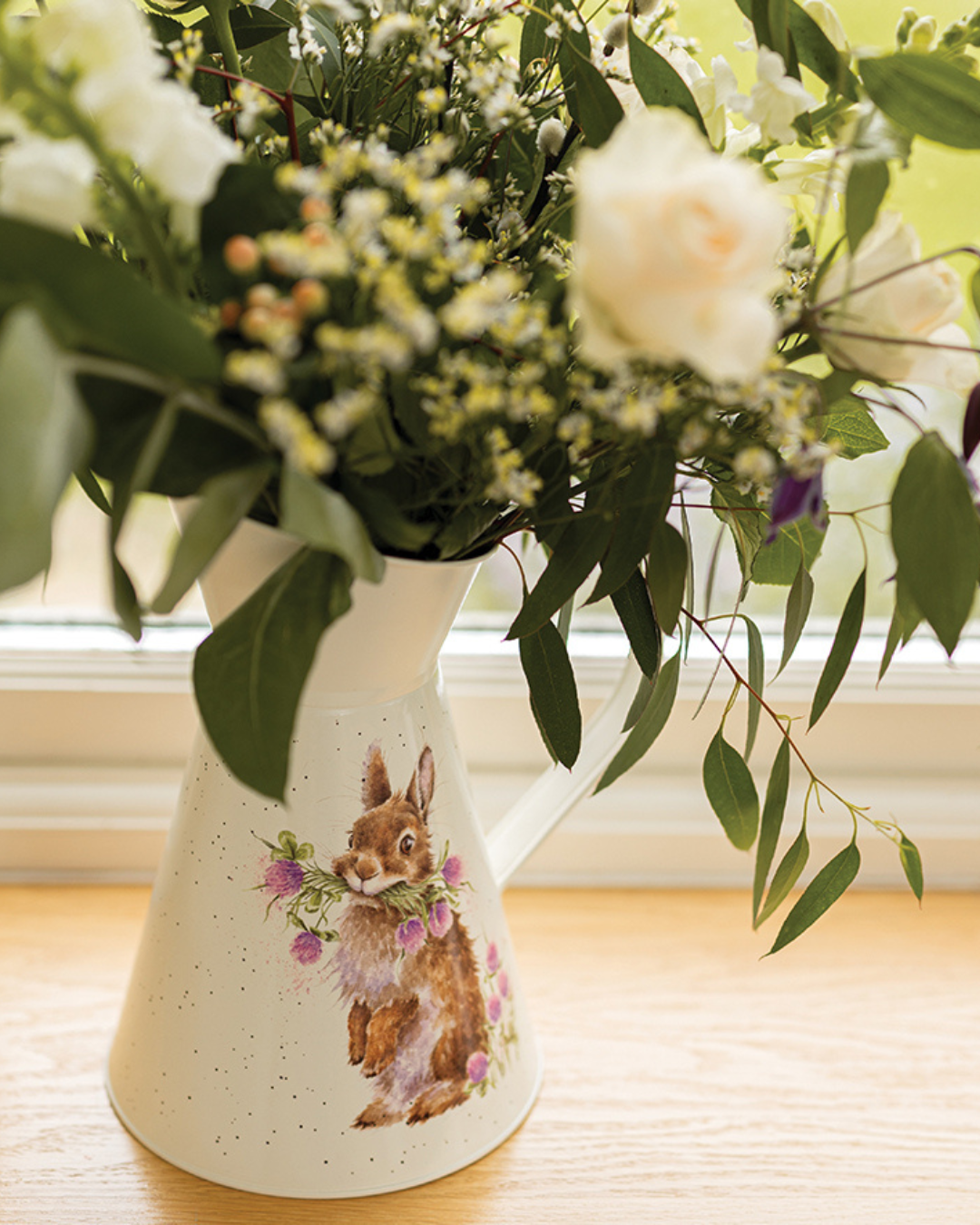 Kaninchen Blumenvase Head Clover Heels Flower Jug von Wrendale Designs auf Holztisch am Fenster dekoriert mit lockerem Blumenstrauß und grünem Blattwerk.