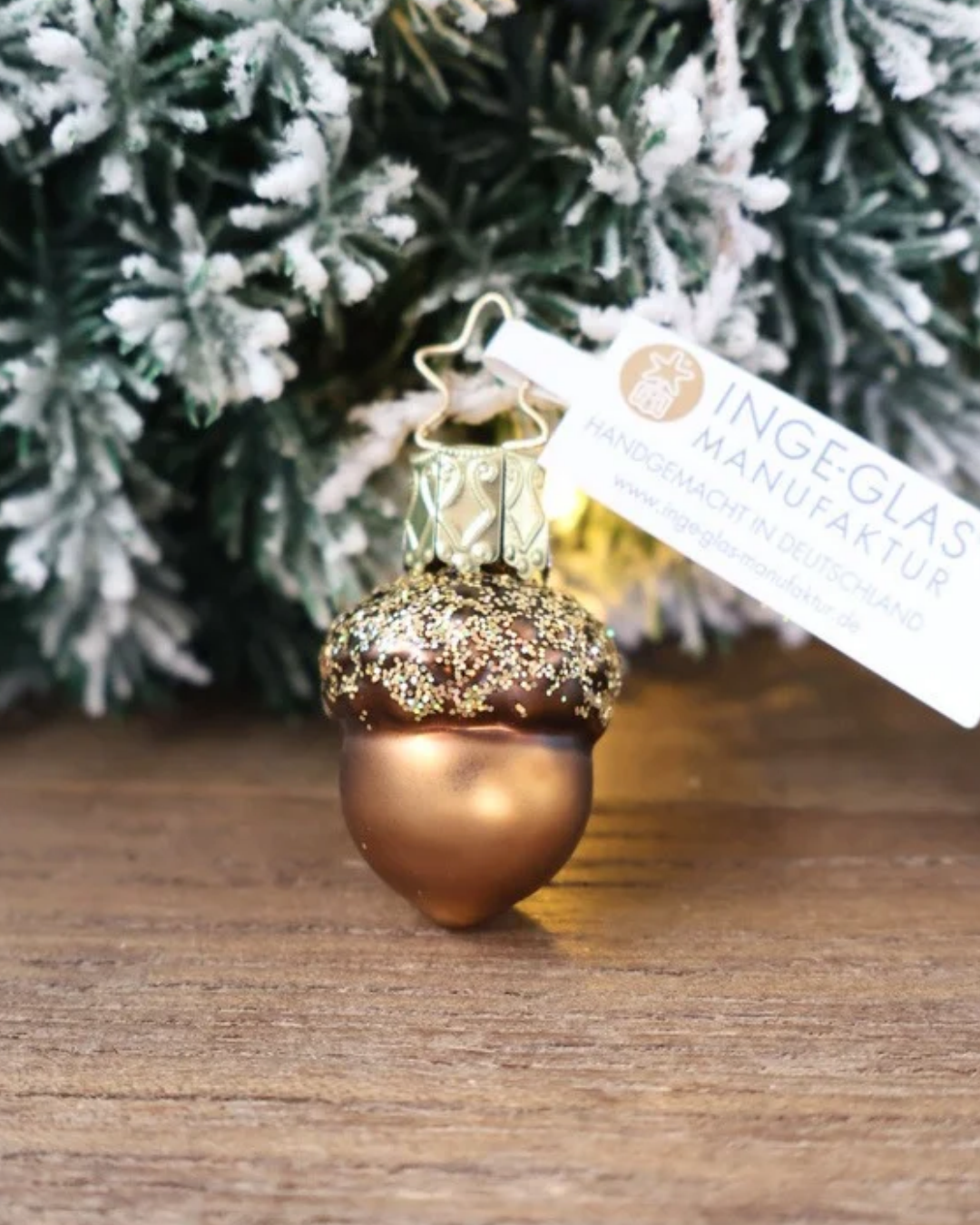 Weihnachtliches kleines Eichel Ornament von Inge Glas dekoriert vor weiß gepudertem Tannengrün auf einem Holztisch.