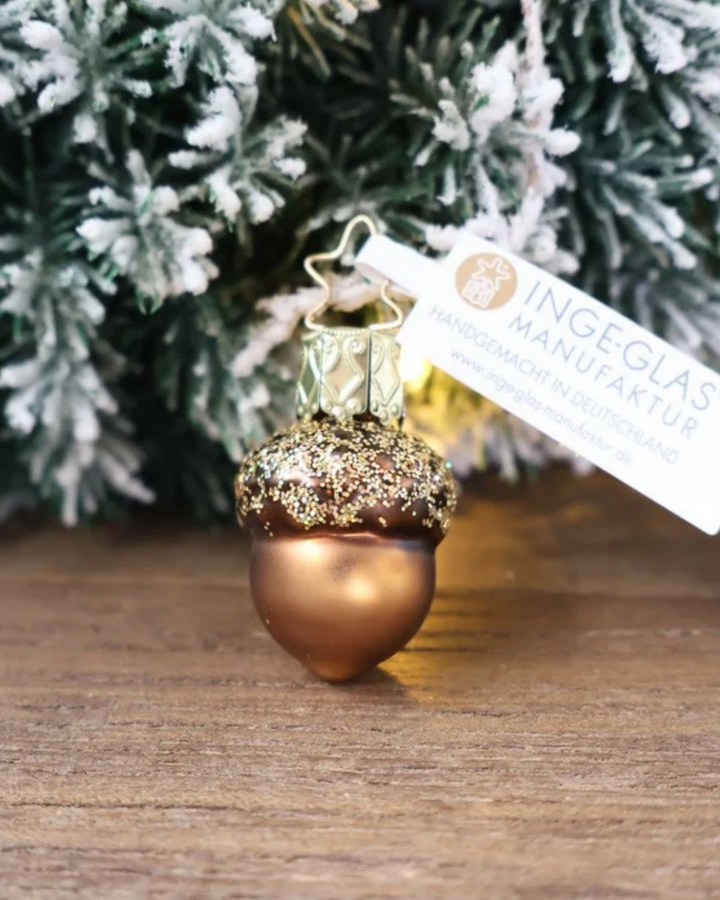 Weihnachtliches kleines Eichel Ornament von Inge Glas dekoriert vor weiß gepudertem Tannengrün auf einem Holztisch.