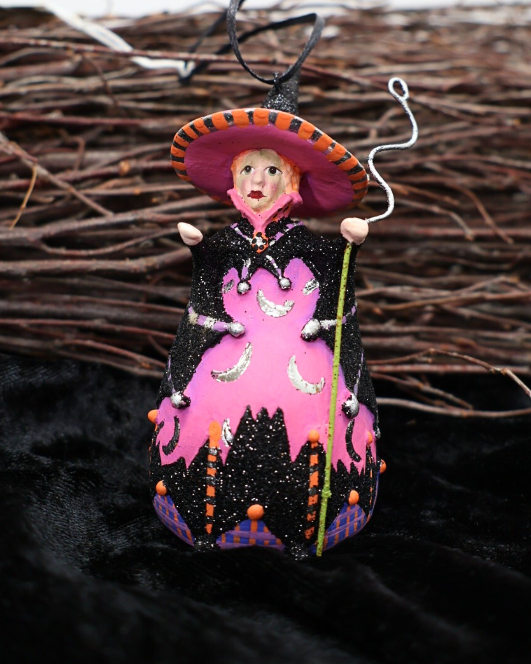 Dekorierte Krinkle Hexen Figur „Mini Bat Moon Witch“ von Patience Brewster als Halloween-Deko vor einem Reisigbesen auf einem schwarzen Samttuch.