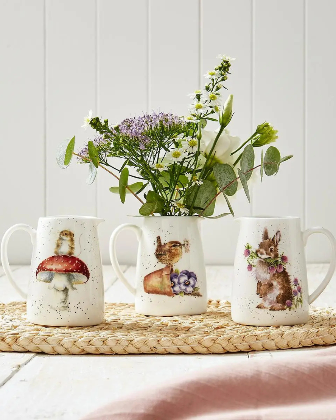 3 Krüge von Wrendale Designs mit einem Maus, Vogel und Hasen Motiv. Der Vogel Krug ist gefüllt mit Blumen und alle 3 Krüge stehen auf einem hellen Holztisch.