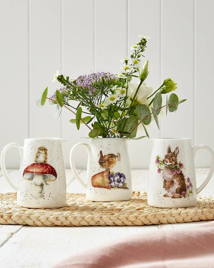 3 Krüge von Wrendale Designs mit einem Maus, Vogel und Hasen Motiv. Der Vogel Krug ist gefüllt mit Blumen und alle 3 Krüge stehen auf einem hellen Holztisch.