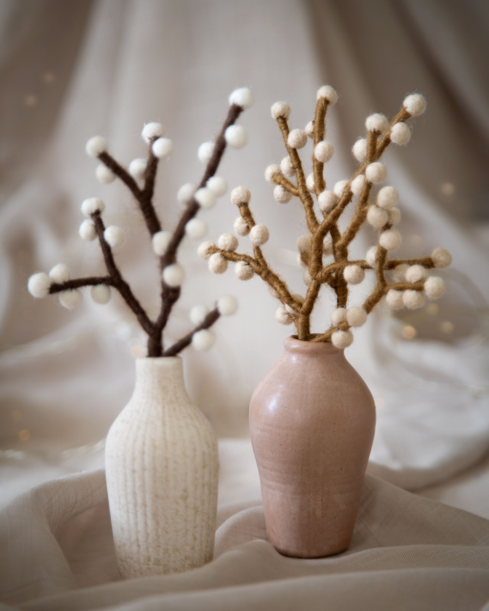 Beiger Mini Beeren-Ast aus Filz von Gry & Sif in einer schlichten Keramikvase arrangiert, weicher Stoffhintergrund in Naturtönen, ruhige und warme Lichtstimmung.