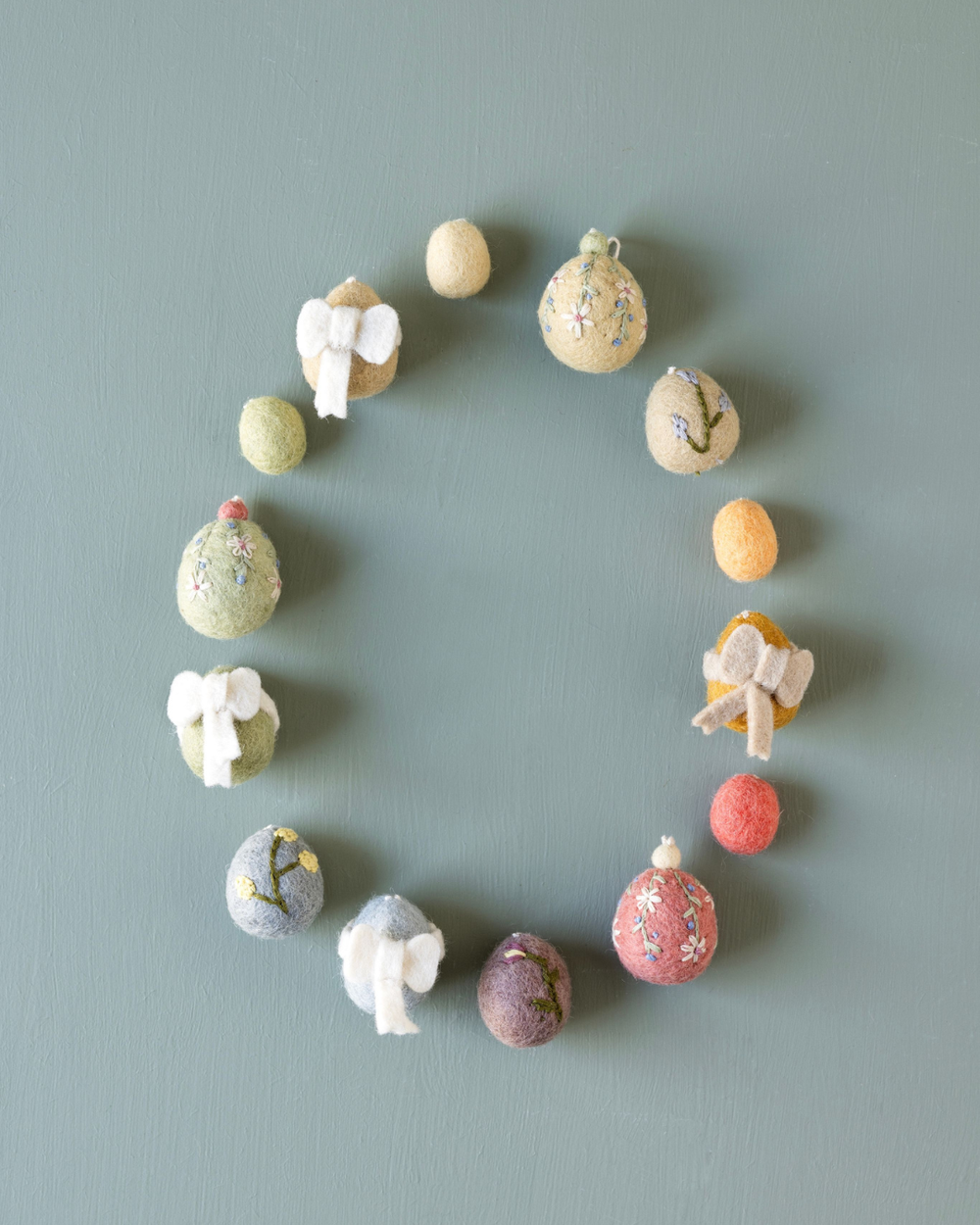 Kranzförmig arrangierte Filz-Ostereier in verschiedenen Farben mit Blumen-Stickereien und Schleifen auf grünem Untergrund.