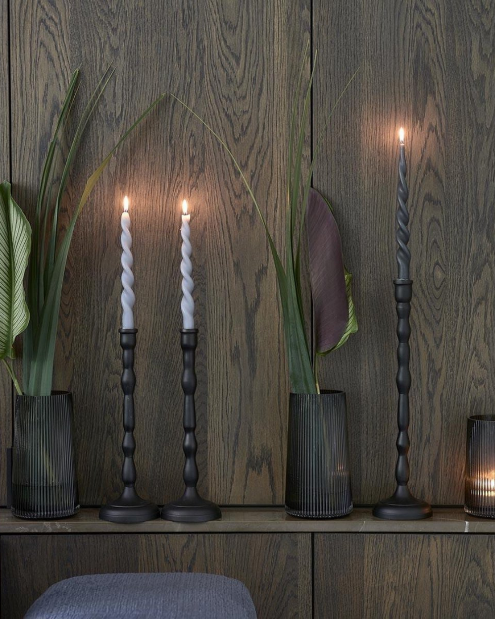 Schwarze Salvador Kerzenständer von Rivièra Maison mit gedrehten Kerzen vor Holzwand.
