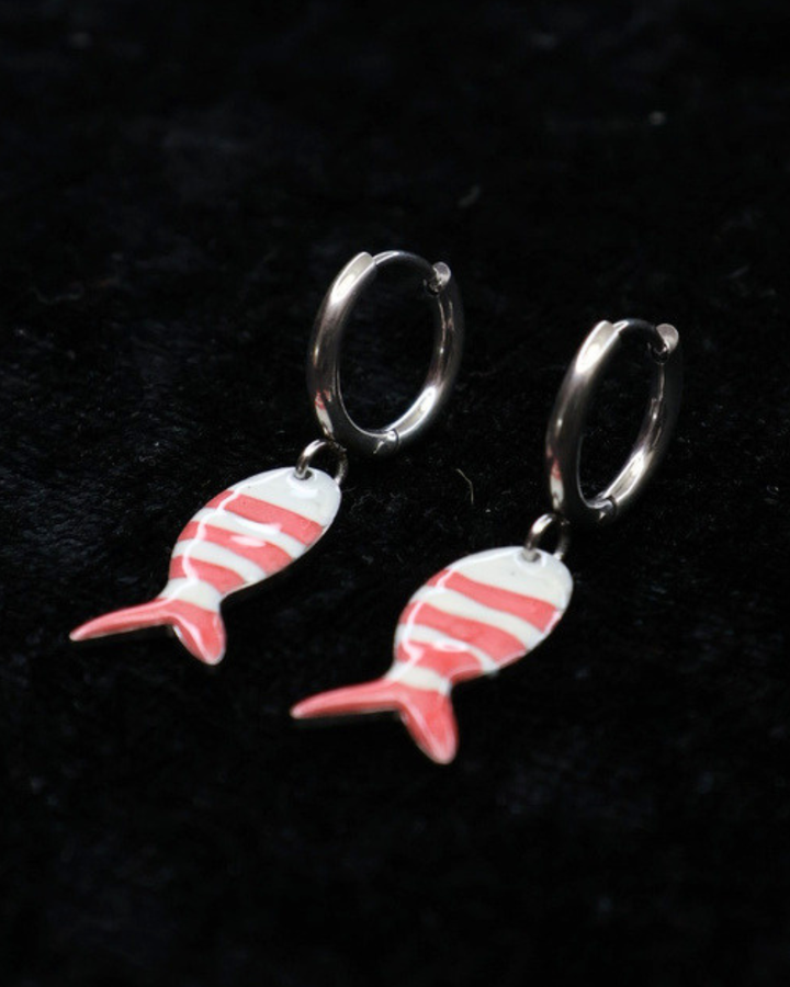 Silberne pink/weiß gestreifte Fisch-Ohrringe von Dottilove auf schwarzer leicht glitzernder Decke.