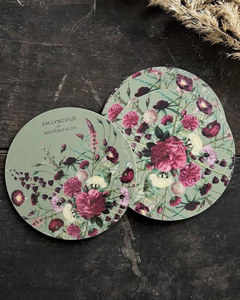 4er Set Untersetzer "Blossom Garden" von Koustrup & co mit farbenfrohen Blumenmotiv auf einem dunklen rauen Holztisch.