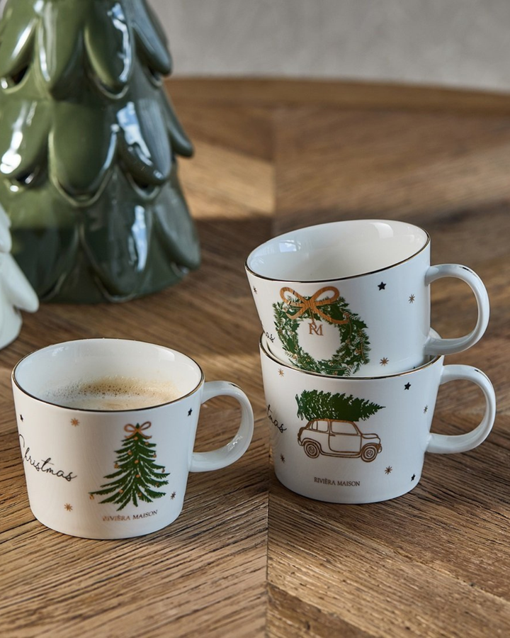 Stimmungsbild: Joyful Christmas Mugs von Rivièra Maison dekorativ gestapelt neben Keramik-Weihnachtsbäumen.