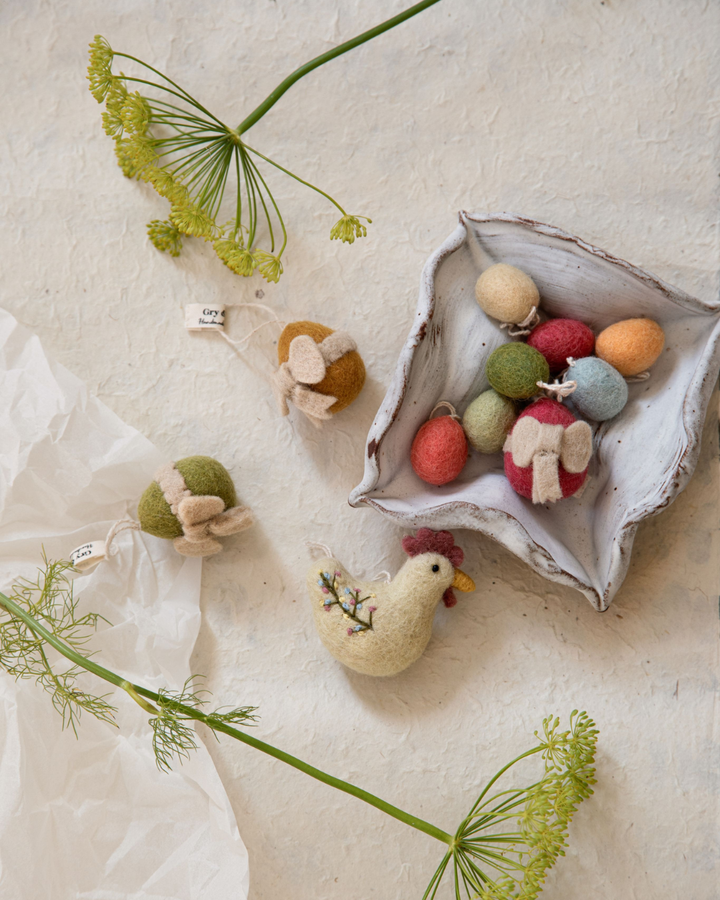 Acht Filz-Ostereier in soften Pastellfarben, locker zusammengebunden mit schwarzem Markenband vor weißem Hintergrund.