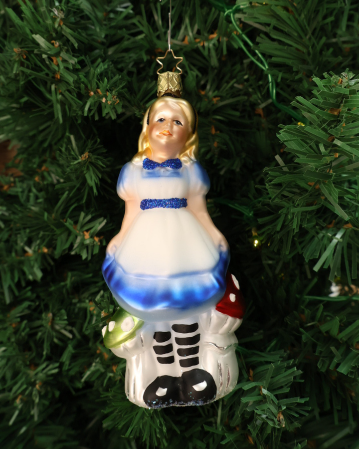Handgefertigte Weihnachtsbaumschnmuckfigur "lice im Wunderland" stehend vor grünen und roten Pilzen- ALice trägt ein weiß-blaues Kleid mit blauem Glitzer Gürtel und Glitzer Fliege. Hier hängend an einem Tannenbaum.