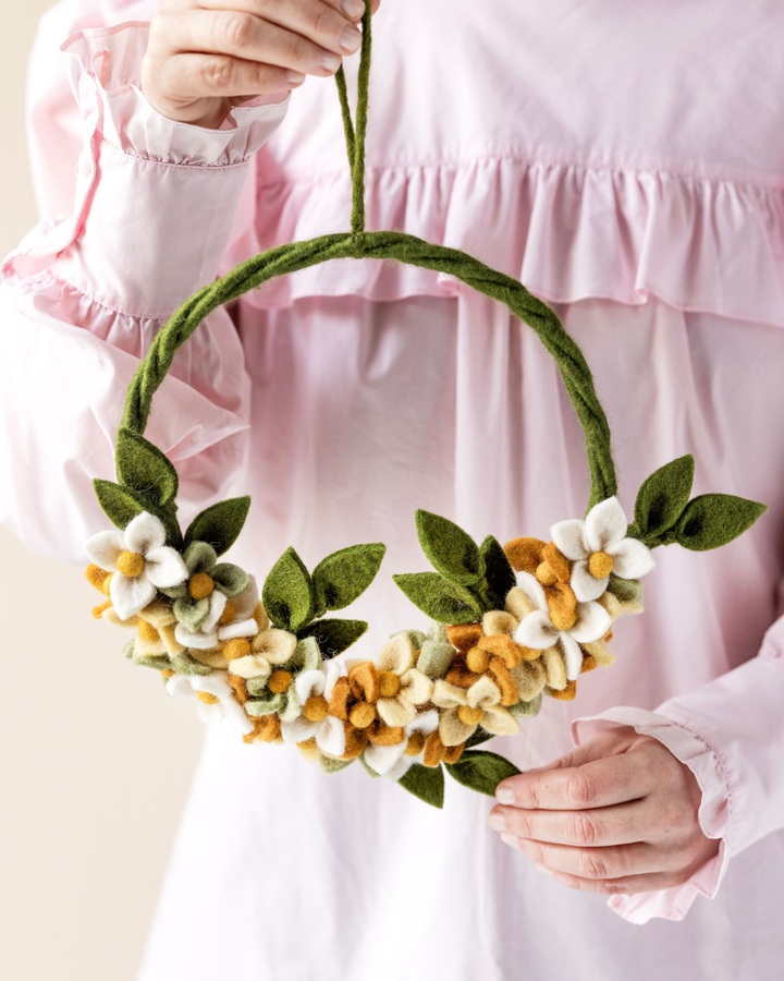 Filzkranz mit Blumen in Gelb-Orange von Gry & Sif, gehalten von einer Person vor hellem Hintergrund. Der Kranz ist am unteren Teil floral dekoriert, die Farben wirken weich und natürlich.