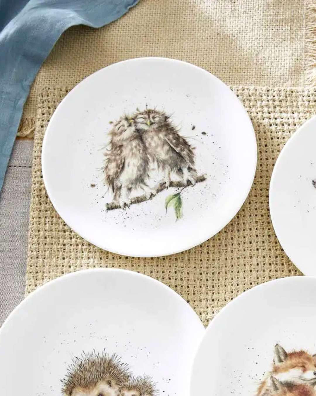 Weißer Eulen Frühstücksteller "Royal Worchester" von Wrendale Designs auf einem bedeckten Tisch. Das Motiv zeigt 2 glücklich kuschelnde Eulen auf einem Ast. 