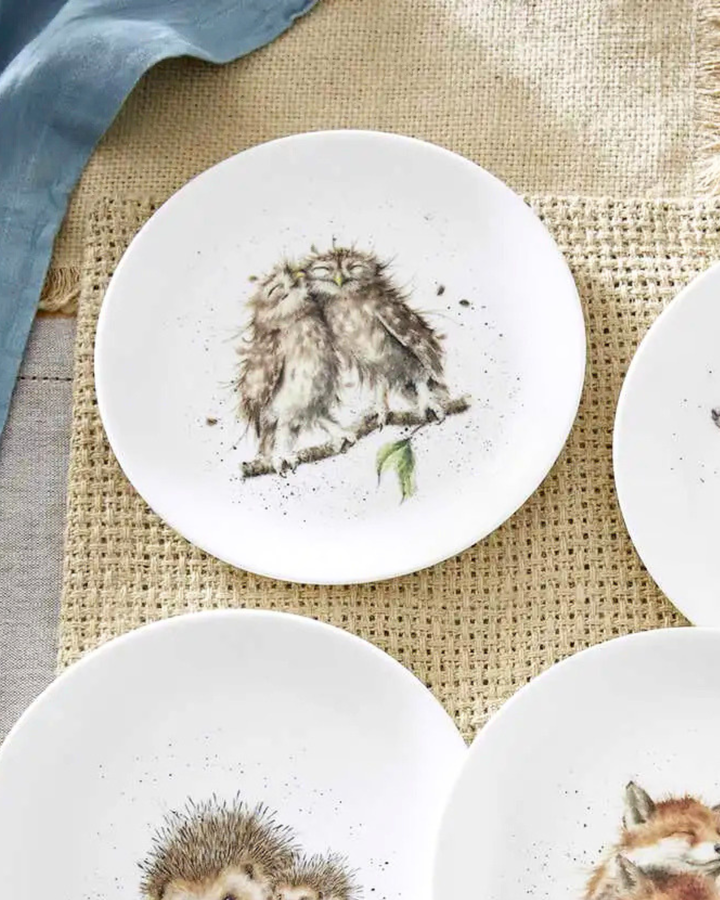 Weißer Eulen Frühstücksteller "Royal Worchester" von Wrendale Designs auf einem bedeckten Tisch. Das Motiv zeigt 2 glücklich kuschelnde Eulen auf einem Ast. 