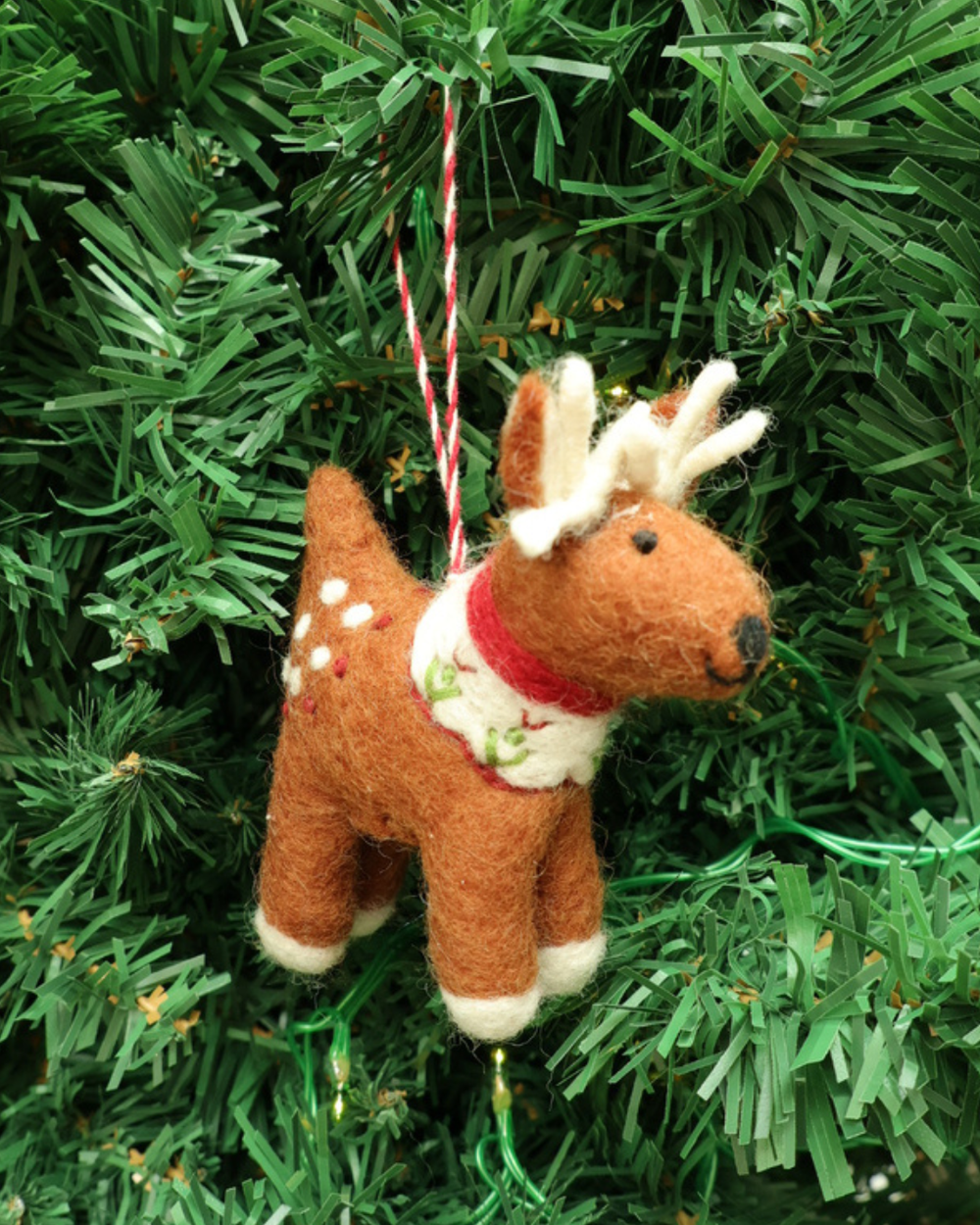 Dekorierter Reh Filzanhänger "Luca" von Grace und Gloria hängt am Tannenbaum. Der Reh ist braun mit weißen Details und trägt einen weiß/roten Schal.