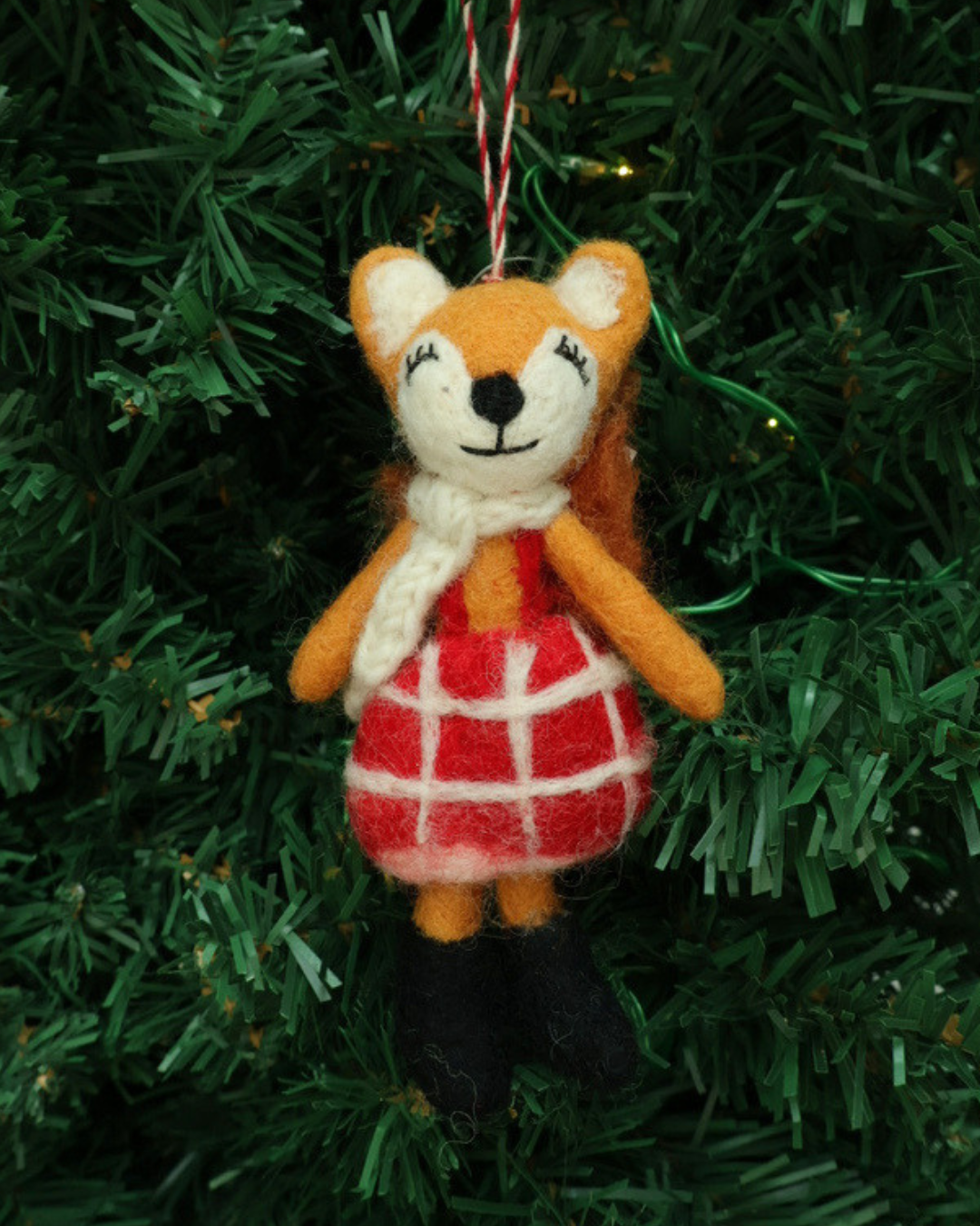 Dekorierter Weihnachts-Fuchs-Filzanhänger "Naomi" von Grace & Gloria hängend an einem Tannenbaum. Es ist ein süßer Fuchs mit einem roten Kleid.