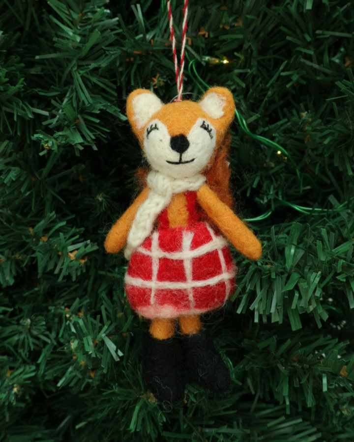 Dekorierter Weihnachts-Fuchs-Filzanhänger "Naomi" von Grace & Gloria hängend an einem Tannenbaum. Es ist ein süßer Fuchs mit einem roten Kleid.