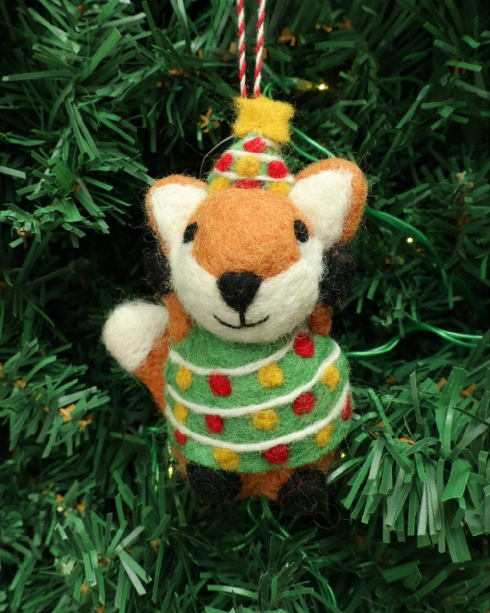Dekorierter Fuchs Weihnachts-Filzanhänger "Tammo" von Grace & Gloria. Der Fuchs hängt an einem Tannenbaum. Er hat ein grünes Oberteil und ein Hut an .
