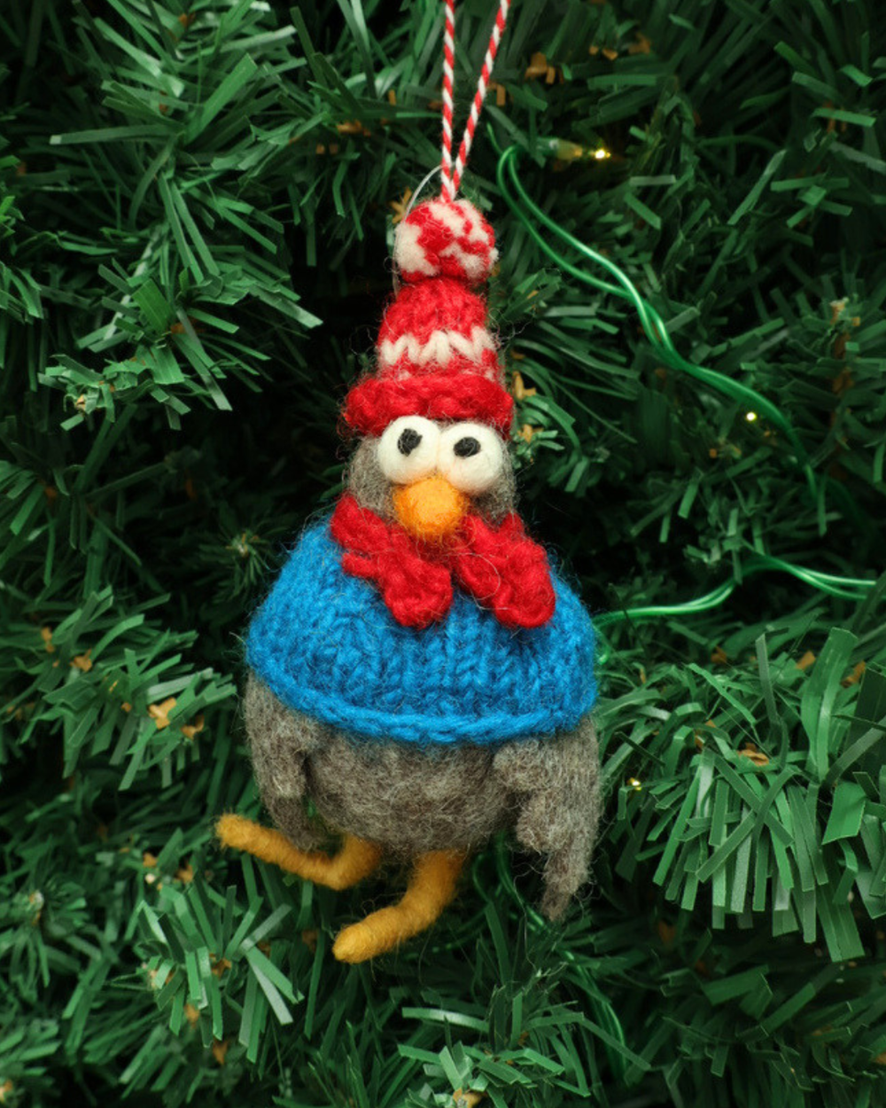 Dekorierter Weihnachts-Hahn- Filzanhänger "Willi" von Grace und Gloria. Der süße graue Hahn Anhänger trägt eine rot/weiß gestreifte Mütze und einen blauen Schal. er Hahn hängt an einem Weihnachtsbaum.