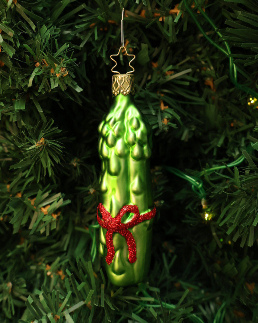 In einem Tannenbaum hängender "Grüner Spargel" mit roter Schleife Weihnachtsbaumschmuck aus Glas zum Aufhängen. In Handarbeit hergestellt von Inge Glas in Deutschland.