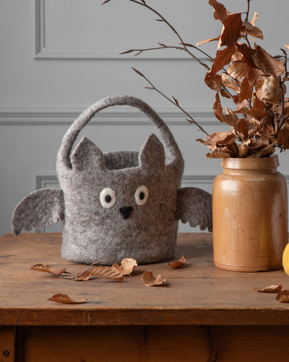 Der Fledermaus Korb für Halloween von Gry & Sif ist auf einem braunen Tisch neben einem braunen Krug mit Ästen darin dekoriert.